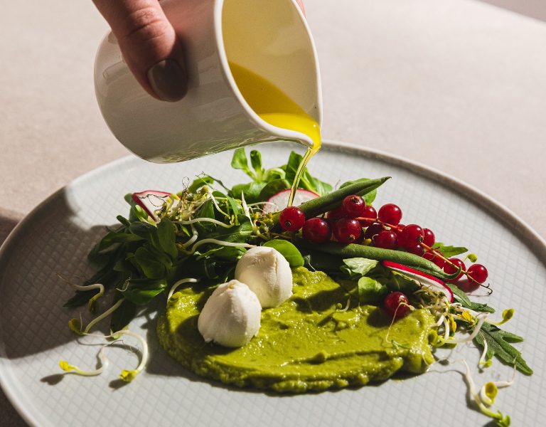 restaurant server pours sauce over a fancy plate of food